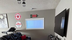 Un soggiorno con un divano in pelle nera, una TV a schermo piatto montata a parete, una ventola a soffitto e un tappeto.