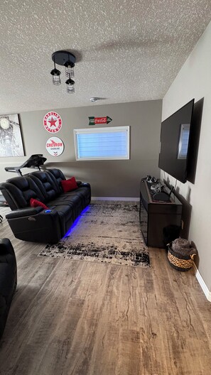 A living room with a black leather couch, a flat-screen TV mounted on the wall, a ceiling fan, and a rug on the floor. - 2 Bedroom 1 bathroom Man cave (Grande Prairie)