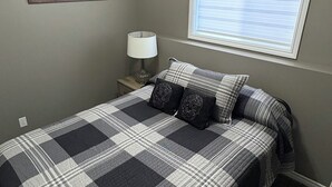 Una camera da letto con un letto, un comodino, una lampada, un lampadario, una finestra con persiane e una mappa appesa al muro.
