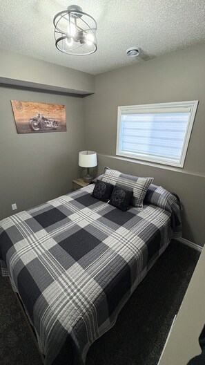 A bedroom with a bed, a nightstand, a lamp, a ceiling light fixture, a window with blinds, and a wall-mounted map. - 2 Bedroom 1 bathroom Man cave (Grande Prairie)