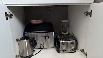 A compact kitchen with white cabinets, a built-in toaster, a kettle, and a blender.