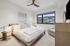 Un dormitorio moderno con cama, lámpara de noche y vistas a edificios a través de una ventana.