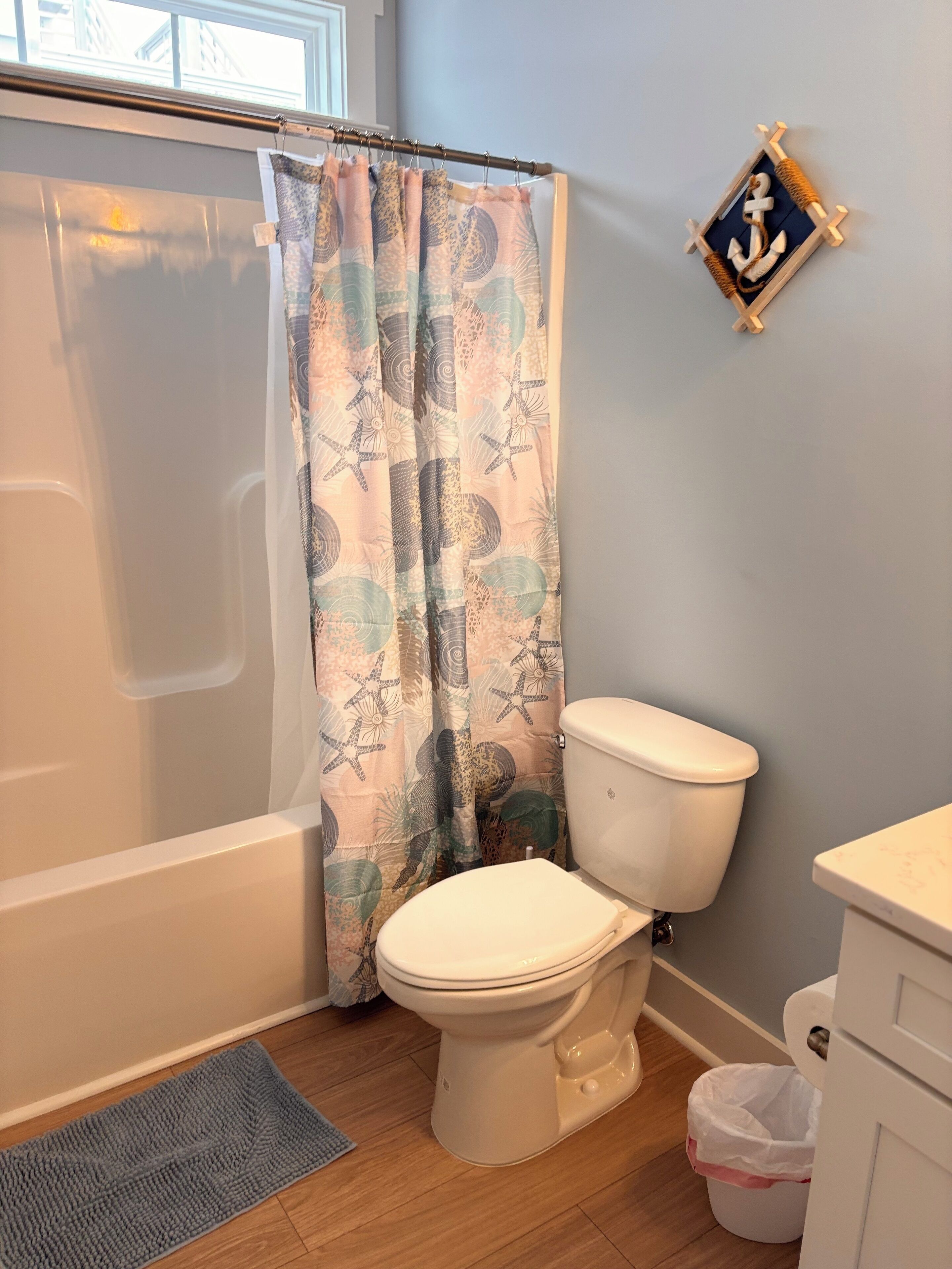 Een badkamer met een bad, toilet en een douchegordijn met een nautisch thema.