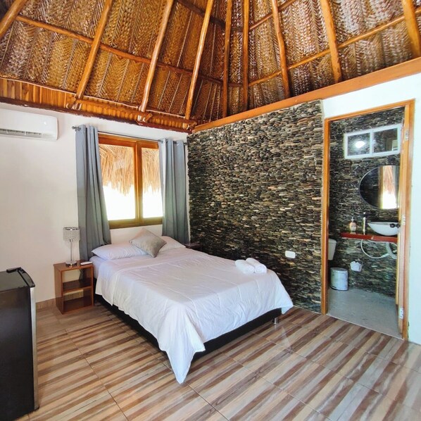 A room with a bed, a small bedside table, a mirror, and a stone wall. - Colibri Parque Tayrona (Santa Marta)