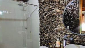 Un bagno con box doccia in vetro, un WC e un lavabo con parete a muro in pietra.