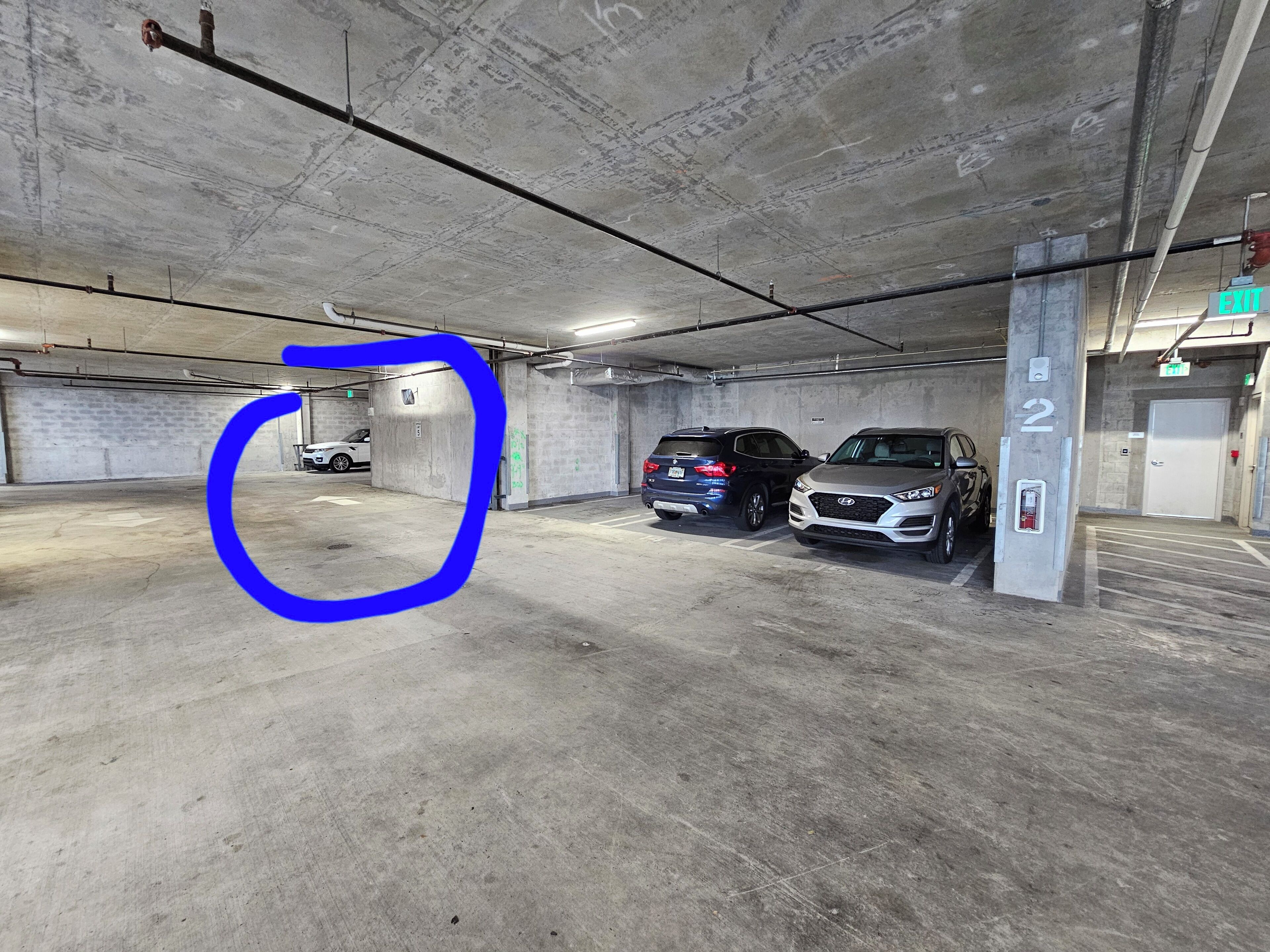 Eine Parkgarage mit Betonwänden, zwei Autos und einem Ausgangsschild.