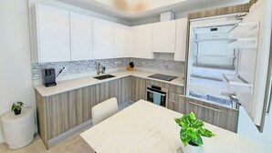 A modern kitchen with white cabinets, a built-in Bosch refrigerator, a sink, and a dining area with a white table and chairs.