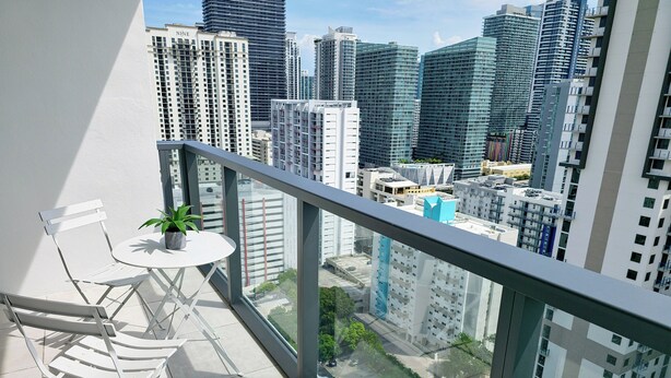 A balcony with a white table and chair, a potted plant, and a city view of high-rise buildings.