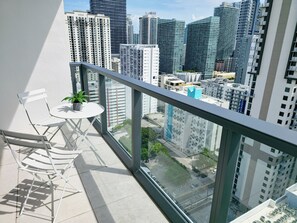 Ein Balkon mit einem weißen Tisch und Stuhl, einem Blumentopf und Blick auf hohe Gebäude der Stadt.