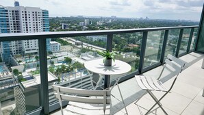 A balcony with a table and chairs, overlooking a cityscape with buildings and greenery.