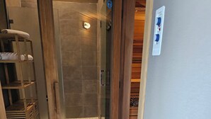 A modern bathroom with a glass-enclosed shower, wooden shelving, and a tiled floor.
