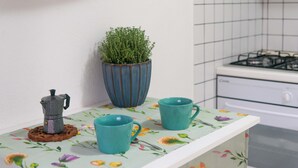 Una encimera de cocina con un molinillo de café, dos tazas azul turquesa y una planta en maceta.