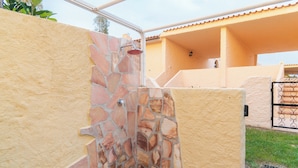 Un cerramiento de ducha de piedra con estructura metálica, junto a una pared color beige y un techo de azulejos.