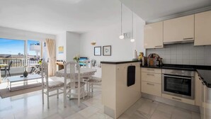 A modern kitchen with a central island, white cabinetry, and a large window overlooking a cityscape. - REF 96 - Charming Apartment with Pool Near Beaches & Golf Courses (Mijas)
