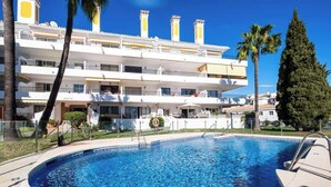 A swimming pool with a clear blue water, surrounded by a white building with balconies and palm trees. - REF 96 - Charming Apartment with Pool Near Beaches & Golf Courses (Mijas)