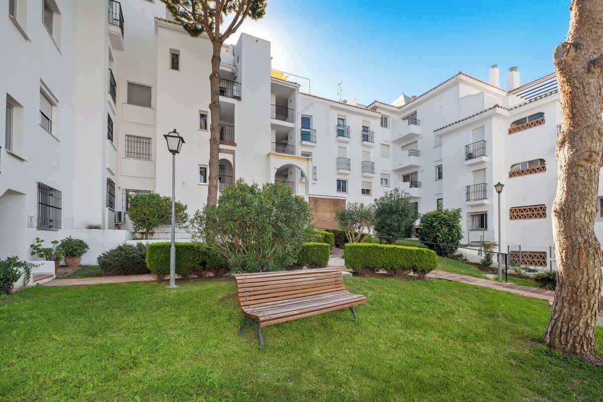 Une cour avec un banc, des haies soigneusement taillées et un bâtiment doté de balcons.