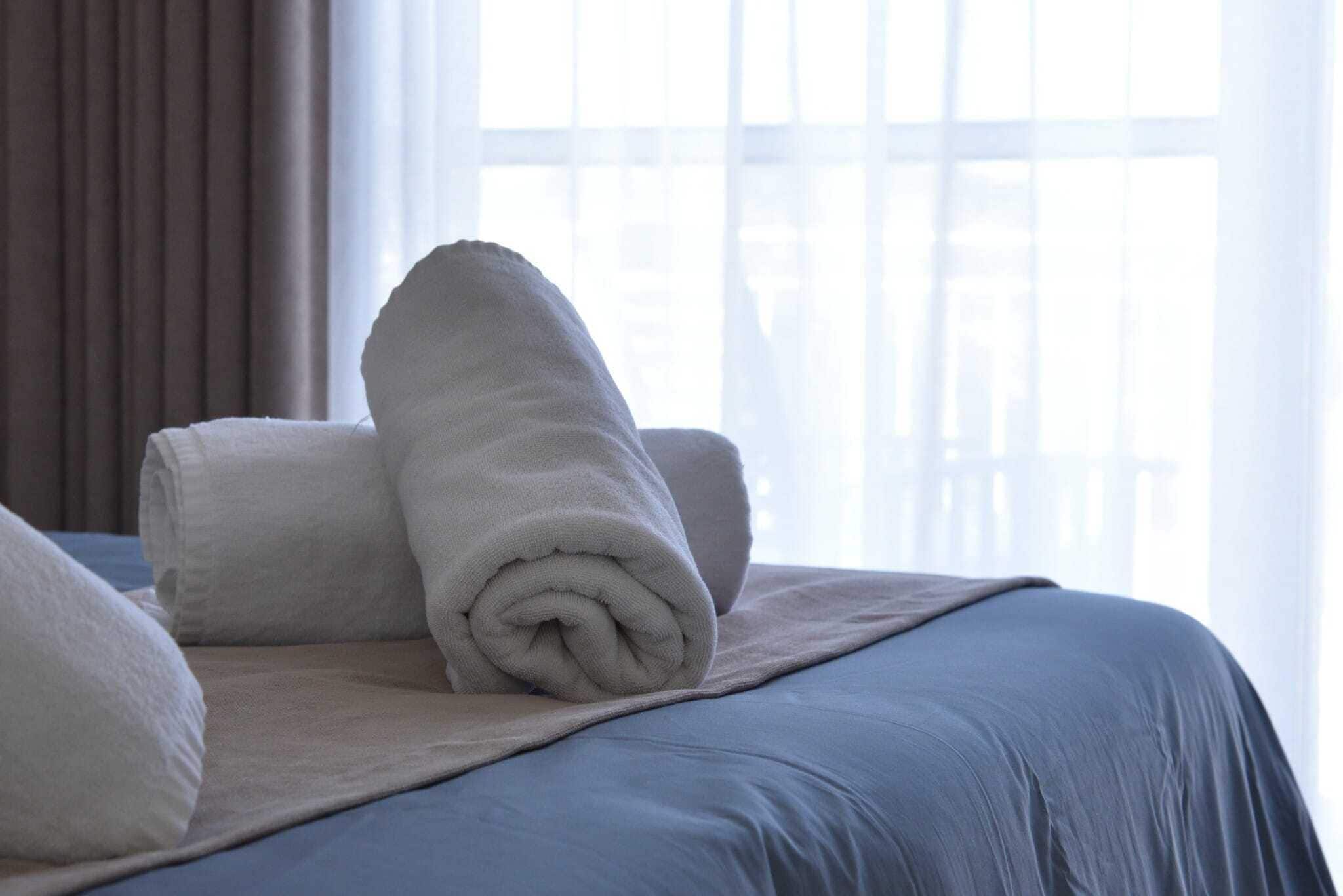 A neatly made bed with rolled white towels and a beige blanket.