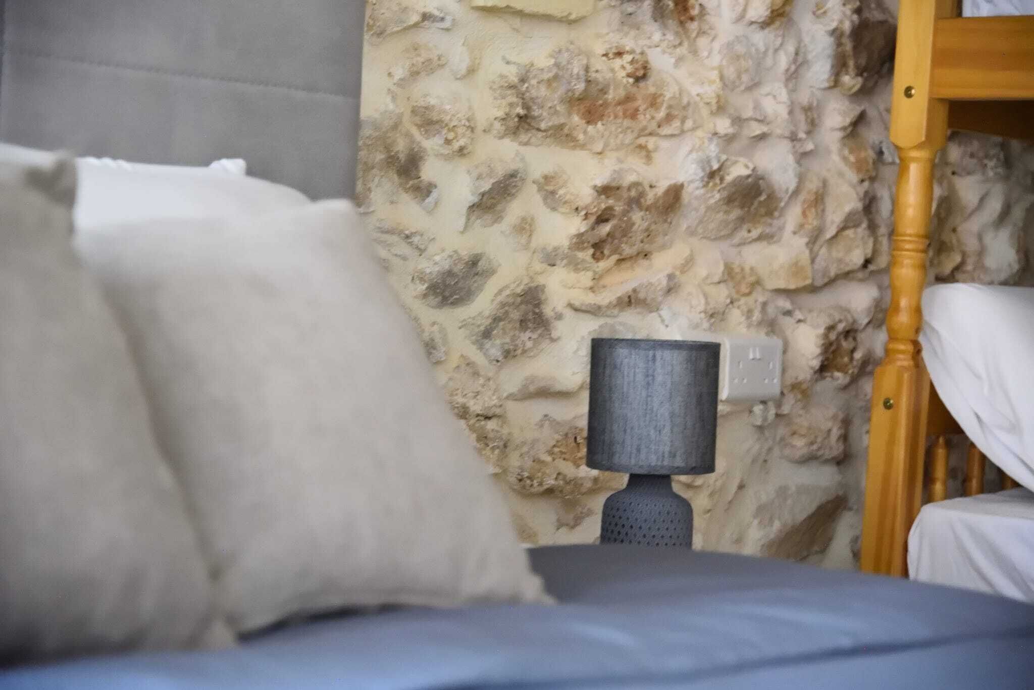 A bed with white bedding, a stone wall, and a wooden headboard.