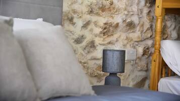A bed with white bedding, a stone wall, and a wooden headboard.