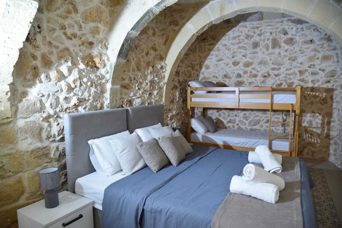 Camera da letto con parete in pietra, un letto a castello, un comodino con una lampada e letti rifatti con cura.