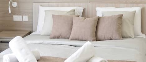 A neatly made bed with beige and white bedding, a wooden headboard, and a bedside table with a lamp and power outlets.