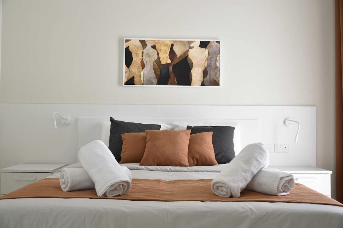 Un letto rifatto con lenzuola bianche e marroni, una coperta marrone e due asciugamani arrotolati.