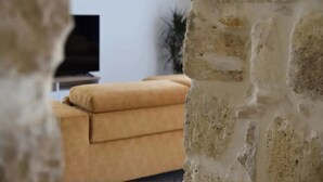 A room with a stone wall, a brown sofa, and a television in the background. - San Pawl bnb Farmhouse Calypso (Xaghra)