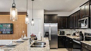 A modern kitchen with granite countertops, stainless steel appliances, dark wooden cabinets, and pendant lighting. - Brand New, Stylish Home 5B/4, 5B, Heated Pool & BBQ (Clermont)