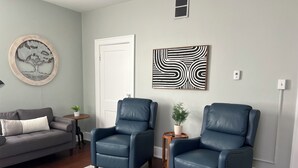 A living room with two blue leather chairs, a grey sofa, a small round table with a plant, and a grey rug.