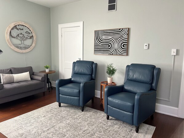 A living room with two blue leather chairs, a grey sofa, a small round table with a plant, and a grey rug.
