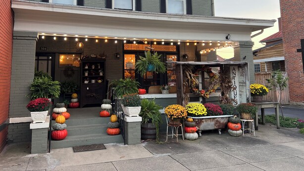 A two-story building with a porch decorated with pumpkins and flowers, string lights, and a sign reading "ANTIQUE."