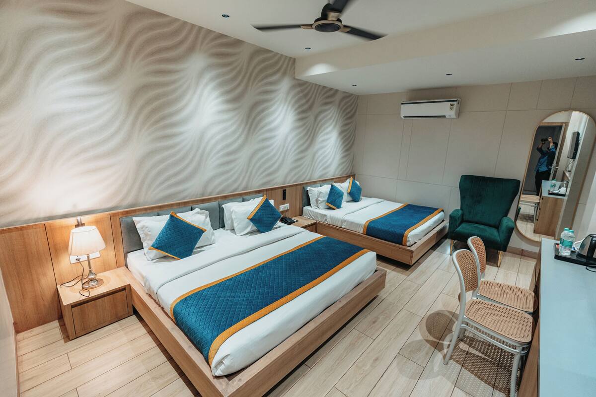 A hotel room with two beds, a desk, a chair, and a mirror.