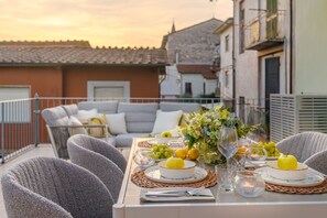 Un tavolo da pranzo apparecchiato con piatti, bicchieri e un vaso di fiori, con un balcone e un divano sullo sfondo.