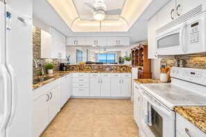 A modern kitchen with white cabinetry, granite countertops, and stainless steel appliances.