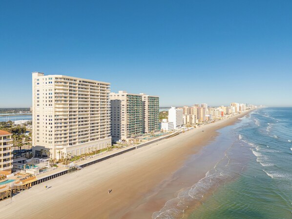 Um hotel à beira-mar com vários edifícios altos, uma praia arenosa e vista clara para o oceano.