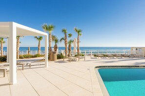 Un espace aménagé au bord de la piscine, offrant une vue dégagée sur l’océan, les palmiers et un coin salon abrité.
