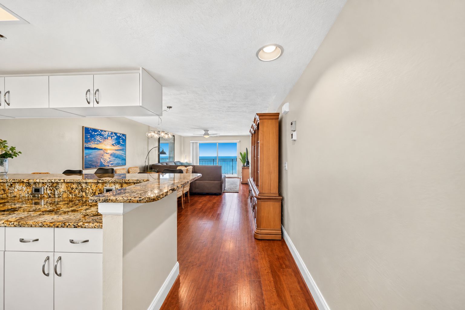 A modern kitchen with white cabinetry, a granite countertop, and a view to the living area.