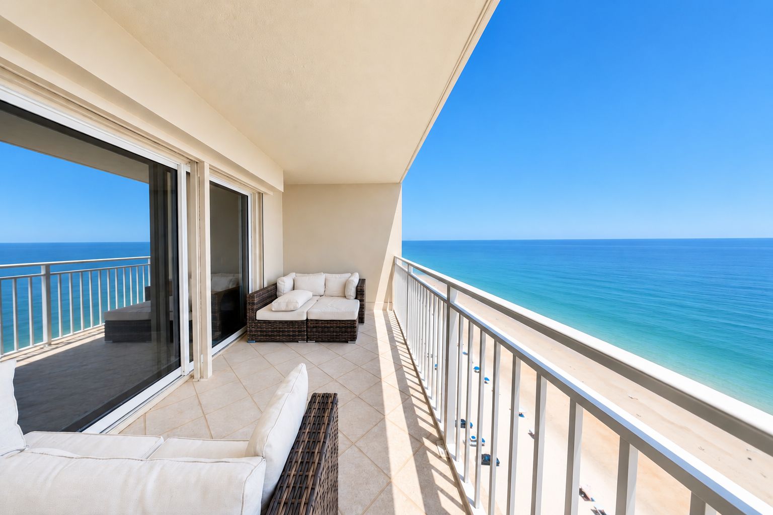 A balcony with a sofa and a chair, overlooking a beach and the sea.