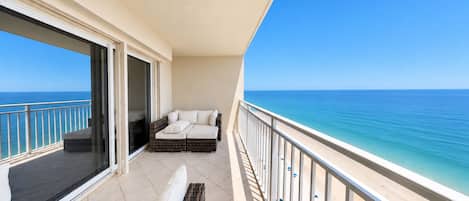 A balcony with a sofa and a chair, overlooking a beach and the sea.