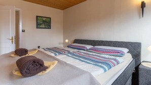 A bedroom with a wooden ceiling, a bed with striped bedding, two towels on the bed, a painting on the wall, and a wall-mounted light fixture. - Ferienhaus in Tönning (Tönning)