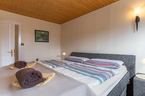 A bedroom with a wooden ceiling, a bed with striped bedding, two towels on the bed, a painting on the wall, and a wall-mounted light fixture. - Ferienhaus in Tönning (Tönning)