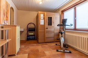 Un sauna avec un banc en bois, un appareil de chauffage mural et une fenêtre équipée de stores.
