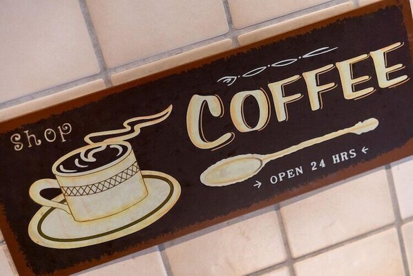 Une enseigne pour un café, représentant une tasse de café et une cuillère, indiquant qu’il est ouvert 24 heures sur 24.