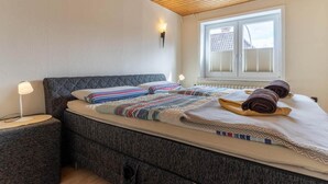 Ein Schlafzimmer mit einem Bett, Nachttischen, einem Fenster mit Jalousien und einer Holzbalkendecke.