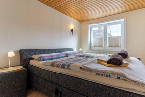 Une chambre à coucher avec un lit, des tables de chevet, une fenêtre avec des stores et un plafond en bois.