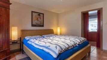 A bedroom with a bed, a nightstand, a lamp, a framed picture on the wall, and a door leading to another room.