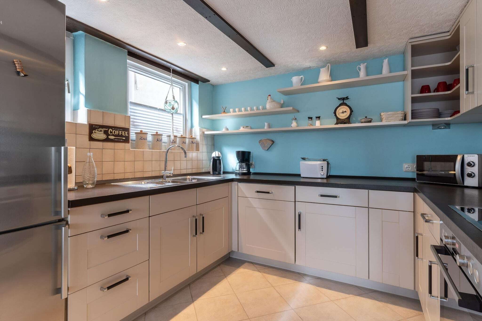 A modern kitchen with white cabinets, a stainless steel refrigerator, a coffee machine, a toaster, and a microwave.