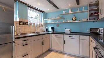 A modern kitchen with white cabinets, a stainless steel refrigerator, a coffee machine, a toaster, and a microwave.