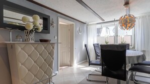 A modern kitchen with a white cabinet, a dining area with a round table and chairs, and a view through a window. - Ferienhaus in Tönning (Tönning)