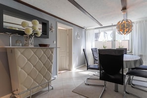 A modern kitchen with a white cabinet, a dining area with a round table and chairs, and a view through a window. - Ferienhaus in Tönning (Tönning)